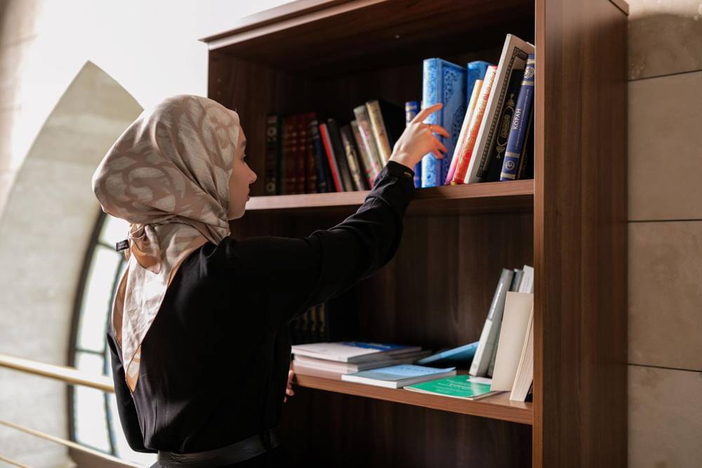 Teacher selecting Islamic books from a bookshelf
